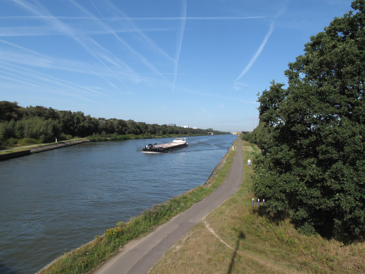 Een geladen vrachtschip op het brede, rechte Albertkanaal, met een fietspad op de dijk